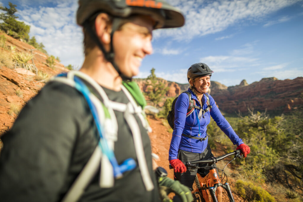 man and woman smiling while on a bike ride through a large red rock formation